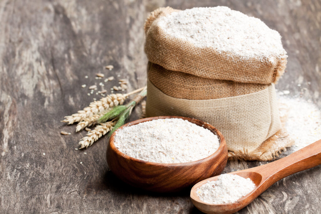 Farine de grains entiers dans un bol en bois et sac de toile à épis